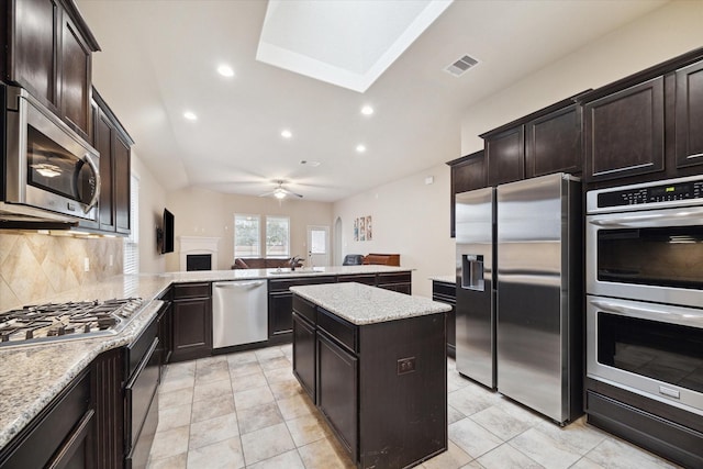 kitchen with appliances with stainless steel finishes, tasteful backsplash, a center island, light stone counters, and kitchen peninsula