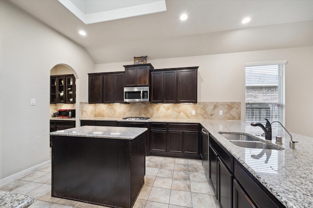 kitchen with sink, light stone counters, tasteful backsplash, a center island, and appliances with stainless steel finishes