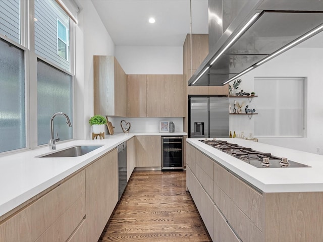 kitchen with sink, appliances with stainless steel finishes, beverage cooler, wall chimney exhaust hood, and light brown cabinets