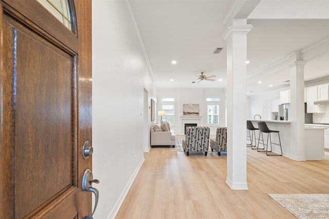 foyer with ceiling fan, ornamental molding, decorative columns, and light wood-type flooring