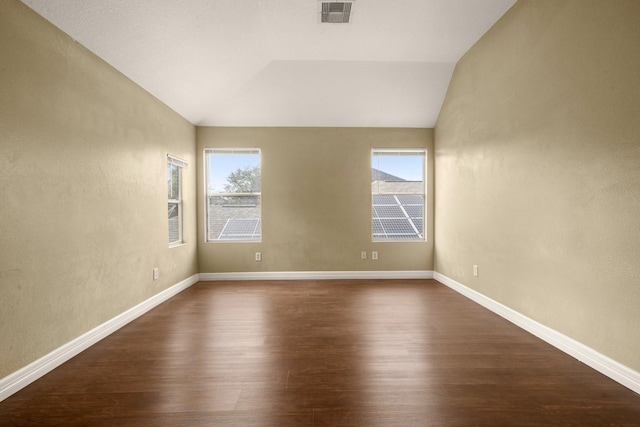 spare room featuring a healthy amount of sunlight, lofted ceiling, and dark wood-type flooring