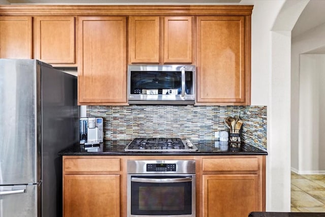 kitchen featuring tasteful backsplash, appliances with stainless steel finishes, tile patterned floors, and dark stone counters