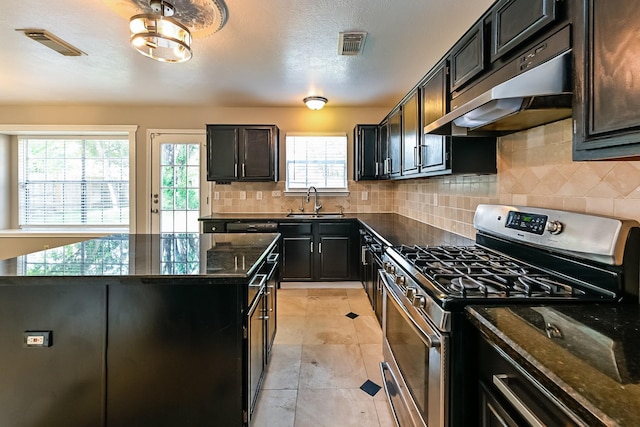 kitchen featuring sink, dark stone countertops, a center island, tasteful backsplash, and gas stove