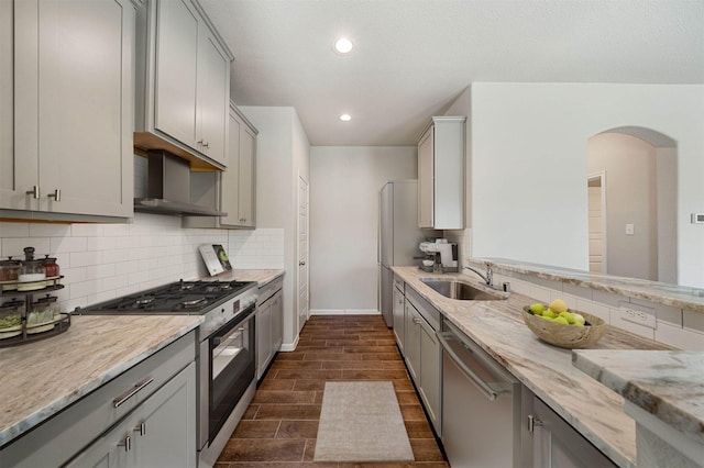 kitchen featuring wall chimney exhaust hood, sink, appliances with stainless steel finishes, gray cabinets, and backsplash