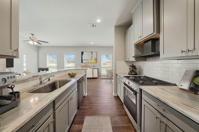 kitchen featuring sink, gray cabinets, appliances with stainless steel finishes, decorative backsplash, and wall chimney exhaust hood