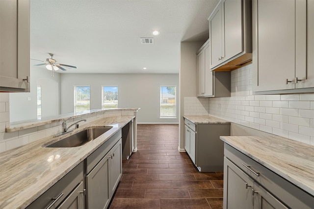 kitchen featuring sink, gray cabinets, ceiling fan, light stone counters, and decorative backsplash