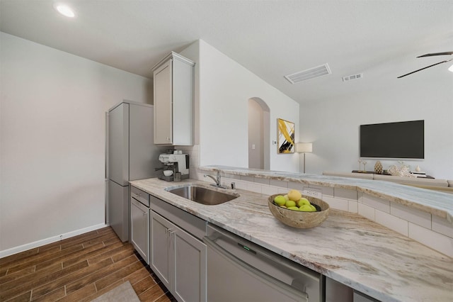 kitchen featuring sink, gray cabinetry, stainless steel dishwasher, ceiling fan, and light stone countertops