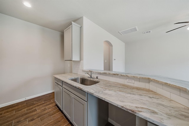 kitchen with sink, tasteful backsplash, gray cabinets, ceiling fan, and light stone countertops