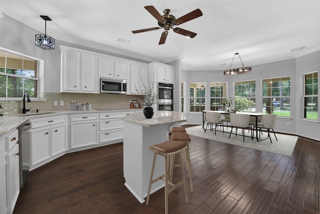 kitchen with a kitchen island, appliances with stainless steel finishes, white cabinets, hanging light fixtures, and crown molding