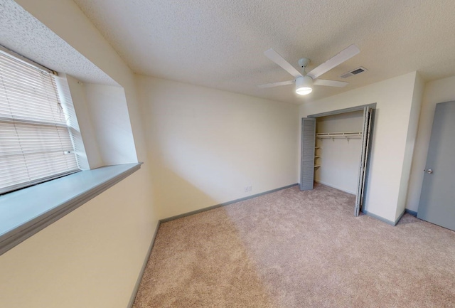 unfurnished bedroom featuring ceiling fan, light colored carpet, a closet, and a textured ceiling