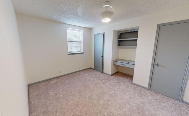 unfurnished bedroom featuring built in desk, light carpet, and a textured ceiling