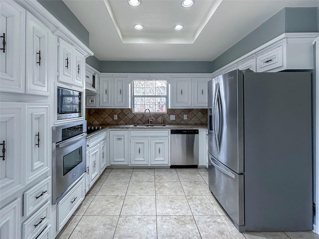 kitchen with light tile patterned flooring, a raised ceiling, sink, white cabinets, and stainless steel appliances