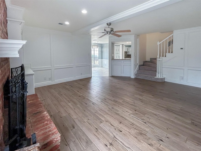 unfurnished living room with ceiling fan, ornamental molding, a fireplace, and light wood-type flooring