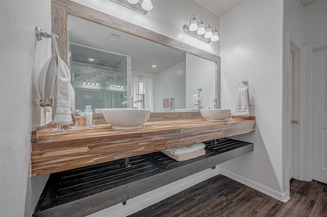 full bath with wood finished floors, a stall shower, double vanity, and baseboards