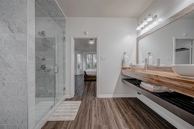 full bathroom featuring wood finished floors, ensuite bathroom, a shower stall, baseboards, and double vanity