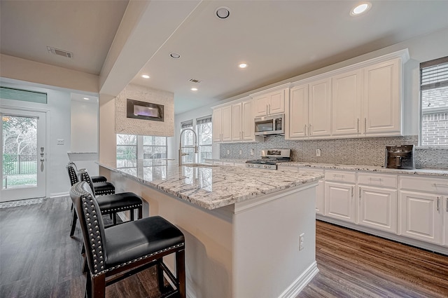 kitchen with appliances with stainless steel finishes, a sink, white cabinets, a breakfast bar, and dark wood-style floors