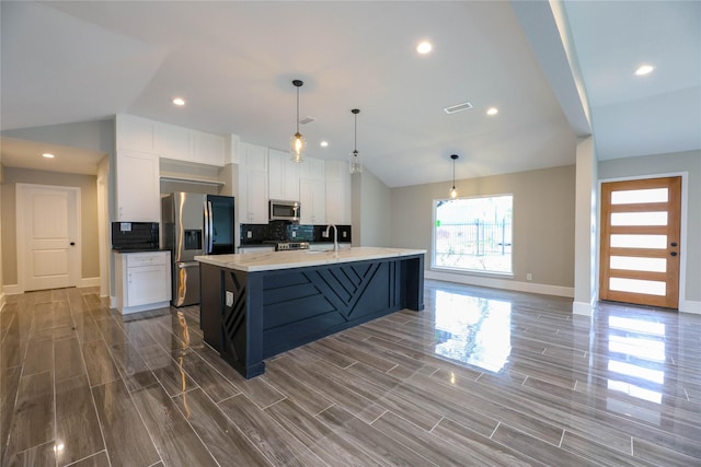 kitchen featuring lofted ceiling, white cabinetry, stainless steel appliances, decorative light fixtures, and a large island with sink