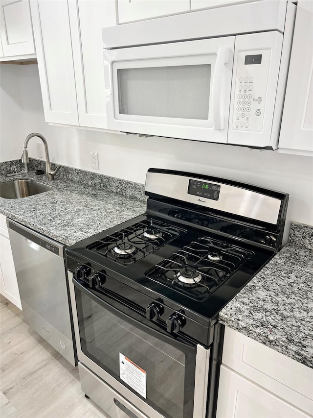 kitchen with sink, stainless steel appliances, white cabinets, and light stone countertops