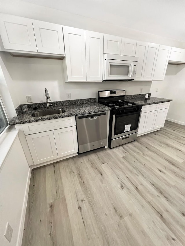 kitchen with stainless steel appliances, dark stone counters, light hardwood / wood-style flooring, and white cabinets