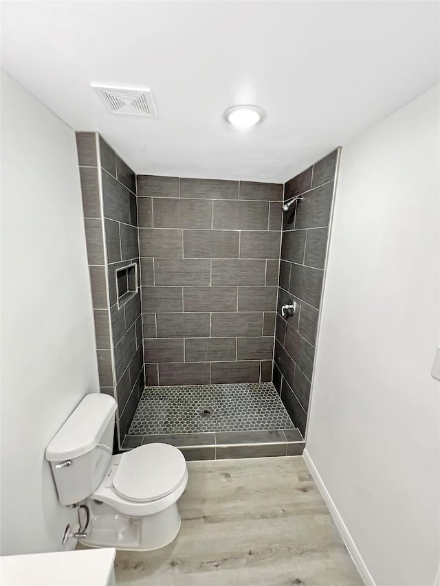 bathroom featuring tiled shower, hardwood / wood-style floors, and toilet