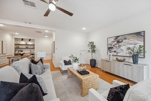 living room with ornamental molding, ceiling fan, built in features, and light hardwood / wood-style floors