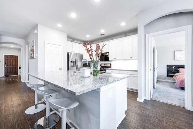 kitchen with stainless steel appliances, light stone countertops, an island with sink, and white cabinets