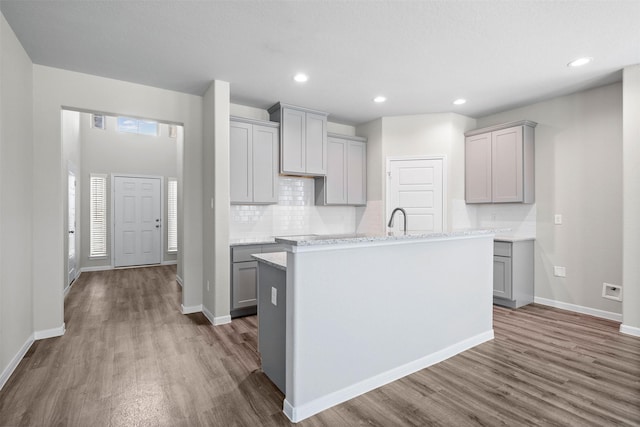 kitchen with sink, gray cabinets, a kitchen island with sink, dark hardwood / wood-style flooring, and decorative backsplash