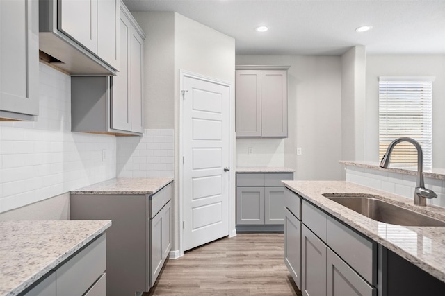 kitchen featuring gray cabinets, tasteful backsplash, sink, light stone counters, and light hardwood / wood-style floors