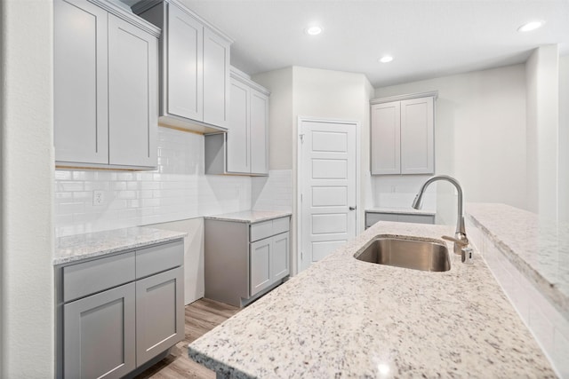 kitchen featuring tasteful backsplash, wood-type flooring, sink, gray cabinetry, and light stone counters