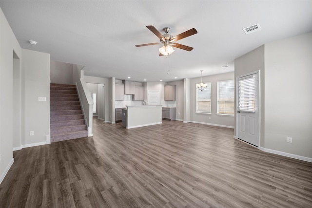 unfurnished living room featuring ceiling fan with notable chandelier and dark hardwood / wood-style floors