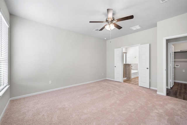 unfurnished bedroom with multiple windows, ensuite bathroom, light carpet, and ceiling fan