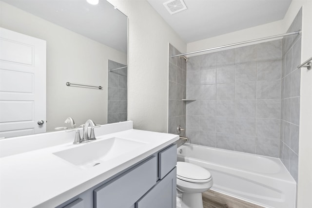 full bathroom with vanity, hardwood / wood-style floors, tiled shower / bath combo, and toilet