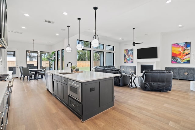 kitchen with sink, hanging light fixtures, light hardwood / wood-style floors, stainless steel appliances, and a center island with sink