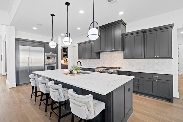 kitchen with sink, light hardwood / wood-style flooring, an island with sink, pendant lighting, and stainless steel appliances