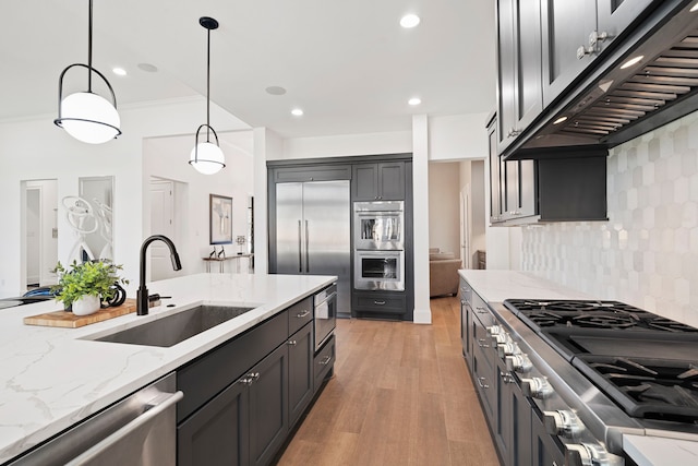 kitchen with sink, extractor fan, light stone counters, built in appliances, and pendant lighting