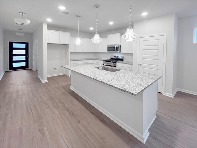 kitchen with appliances with stainless steel finishes, a center island with sink, white cabinets, and light stone counters