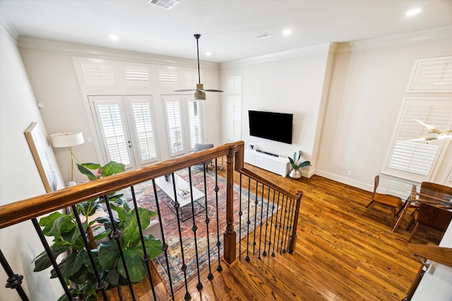 hall with baseboards, visible vents, wood finished floors, crown molding, and an upstairs landing