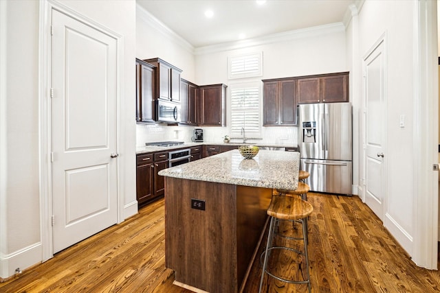 kitchen with dark wood-style floors, crown molding, stainless steel appliances, a kitchen island, and dark brown cabinets