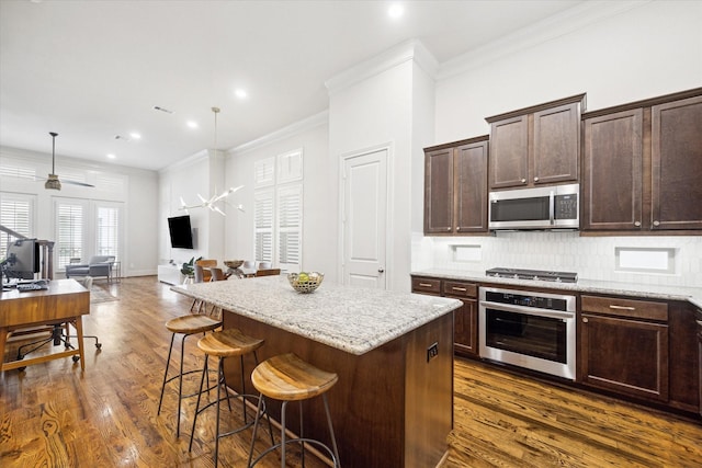 kitchen with dark brown cabinetry, stainless steel appliances, a kitchen breakfast bar, open floor plan, and ornamental molding