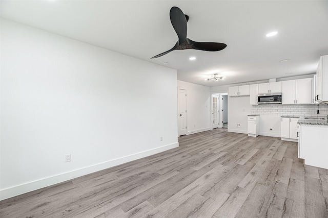 kitchen featuring sink, white cabinetry, light stone counters, ceiling fan, and backsplash