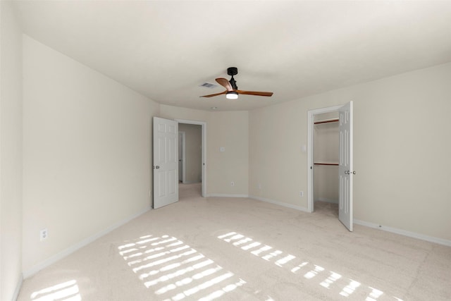 unfurnished bedroom with a walk in closet, light colored carpet, a closet, and ceiling fan