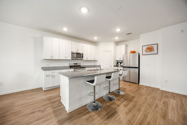 kitchen featuring light stone countertops, white cabinetry, appliances with stainless steel finishes, and a center island with sink