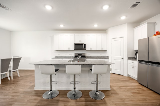 kitchen with a breakfast bar, white cabinetry, appliances with stainless steel finishes, an island with sink, and light stone countertops