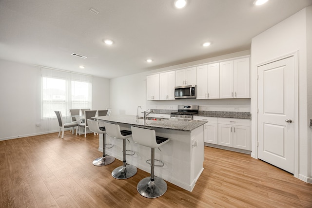 kitchen with sink, stone countertops, an island with sink, stainless steel appliances, and white cabinets