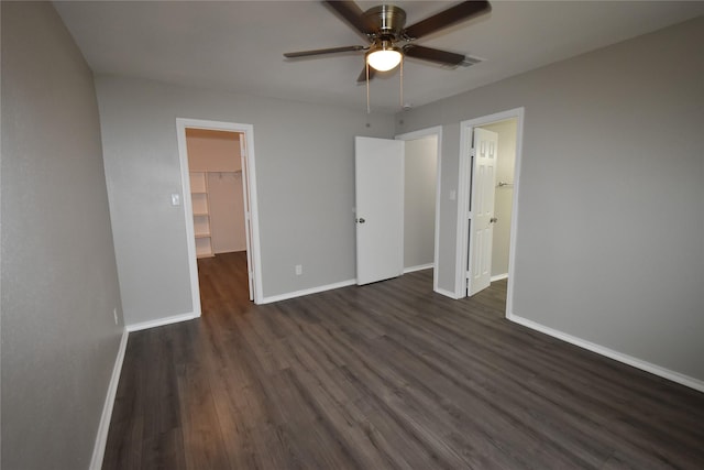 unfurnished bedroom featuring a walk in closet, dark wood-type flooring, a closet, baseboards, and ceiling fan