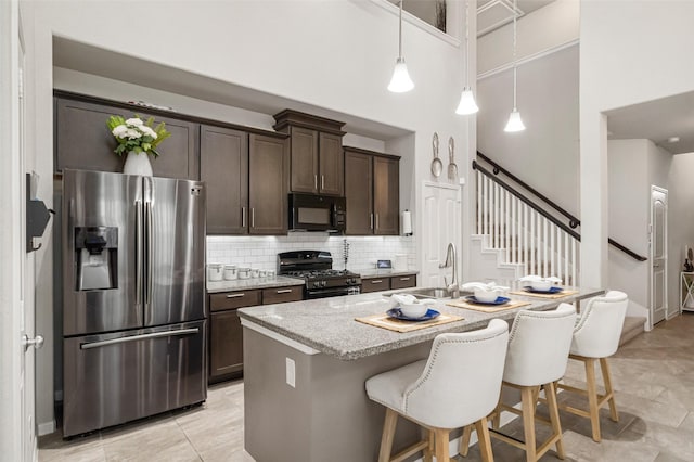 kitchen featuring dark brown cabinets, black microwave, range with gas stovetop, stainless steel fridge, and a sink