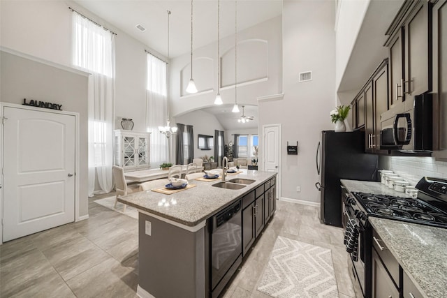 kitchen with dishwashing machine, light stone counters, a kitchen island with sink, a sink, and range with gas cooktop