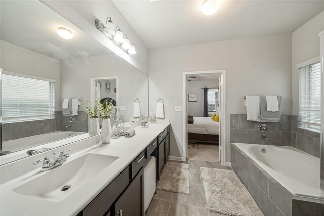 full bathroom featuring a bath, double vanity, ensuite bath, and a sink