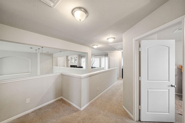 hallway featuring baseboards, light carpet, a textured ceiling, and visible vents