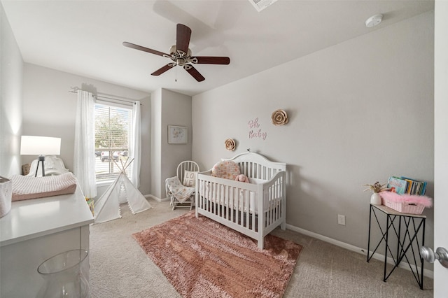 bedroom with a nursery area, baseboards, carpet floors, and ceiling fan